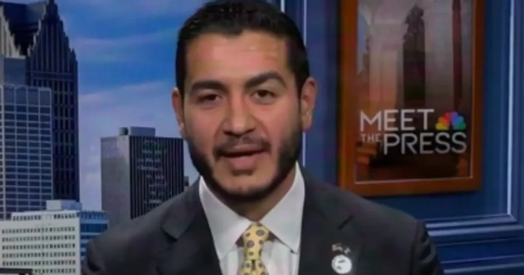 The image shows a man in a suit and tie on a news program set, with the "Meet the Press" logo visible in the background.