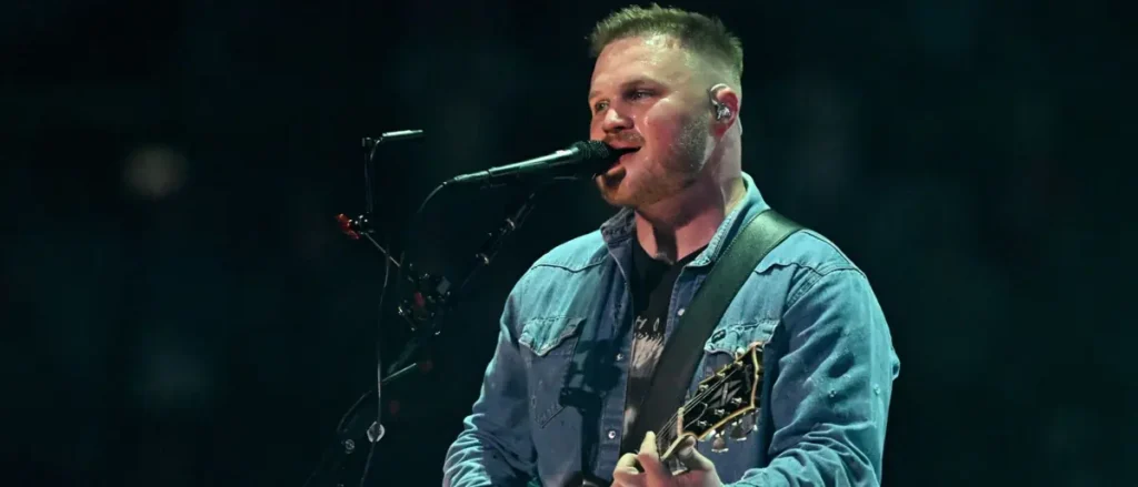 A musician is performing on stage, singing into a microphone while holding a guitar.