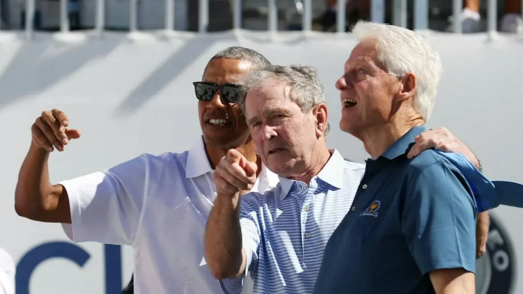 The photo shows three former U.S. presidents, including Barack Obama, George W. Bush, and Bill Clinton, posing together at an outdoor event.