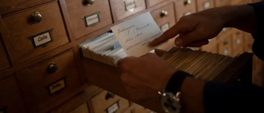 A person is searching through a card catalog, holding a card labeled "Echarri (Granito) Año 1804."
