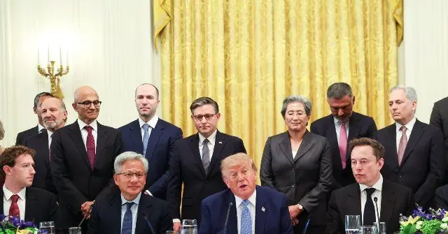 The photo shows a formal meeting with a group of individuals in suits, seated and standing, in what appears to be a formal setting, possibly a government or official event.