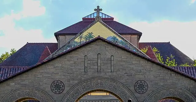 The image shows the front facade of a church with a cross on top, featuring intricate architectural details and a decorative mural above the entrance.