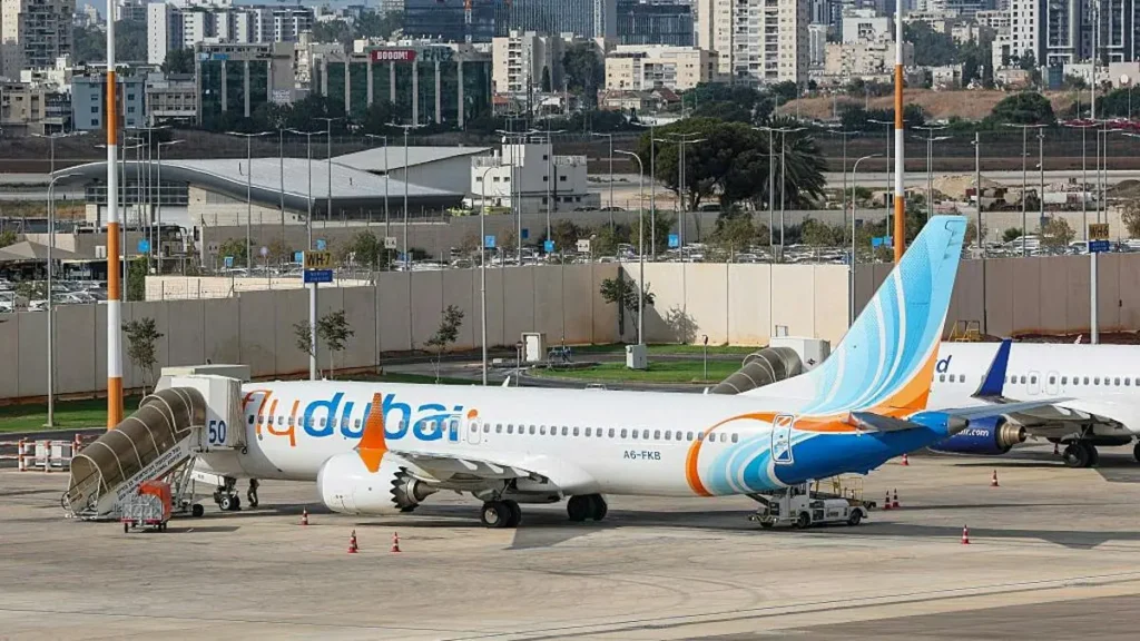A flydubai aircraft is parked on the tarmac at an airport, with a cityscape in the background.