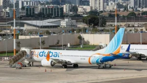 A flydubai aircraft is parked on the tarmac at an airport, with a cityscape in the background.