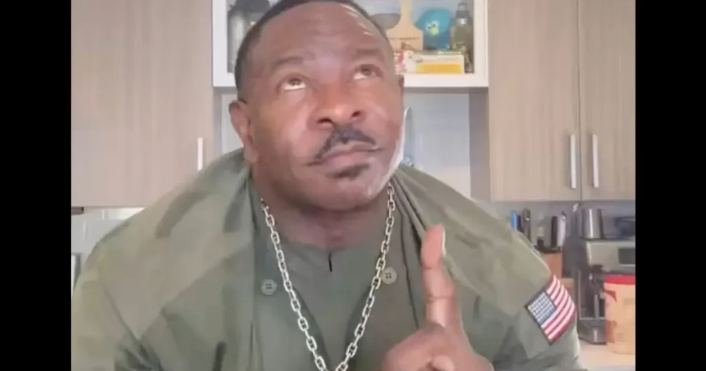 The image shows a man in a green military-style jacket giving a thumbs-up gesture in a kitchen setting.