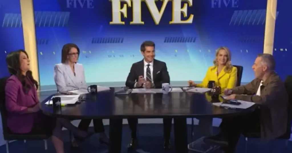 A group of five people are seated around a table in a news studio, engaged in a discussion.