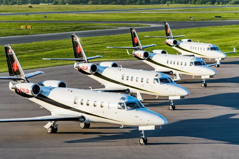 A row of private jets is parked on an airport tarmac under clear skies.