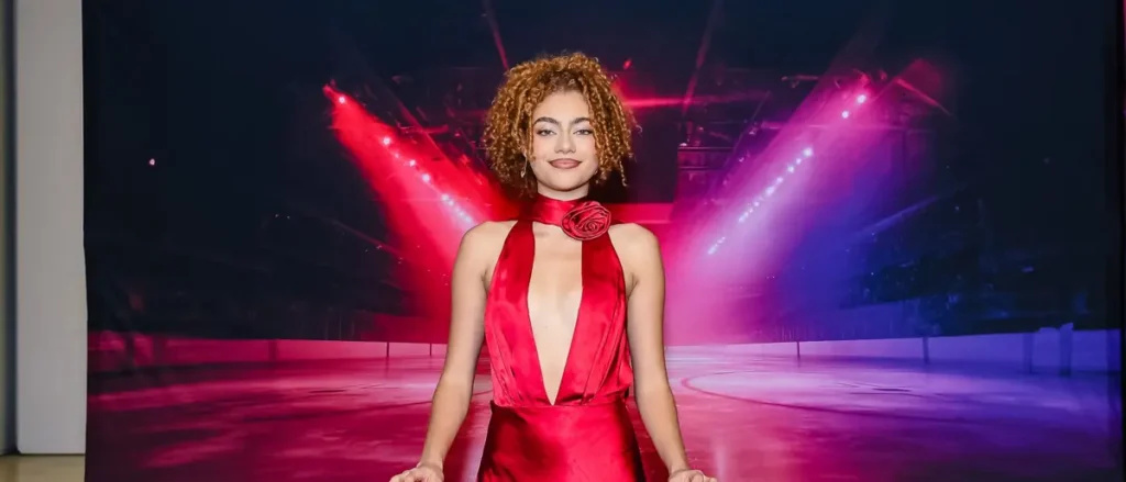 A person in a red dress stands on a stage with vibrant red and purple lighting in the background.