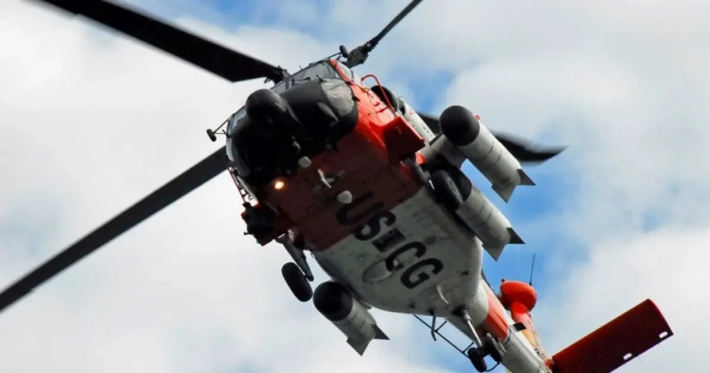 A U.S. Coast Guard helicopter is captured in flight against a cloudy sky.
