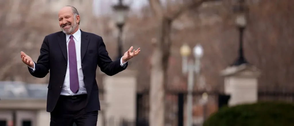 A man in a suit and tie stands with his arms outstretched in an outdoor setting.