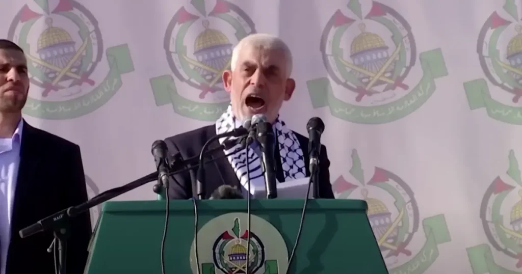 A man stands at a podium with microphones, speaking in front of a backdrop featuring the emblem of the Palestinian Authority.