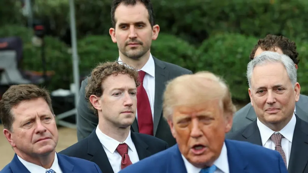 The image shows a group of men in suits, with one man speaking in the foreground while others listen attentively.