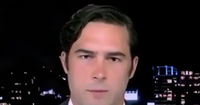 The image shows a news anchor in front of a cityscape backdrop.