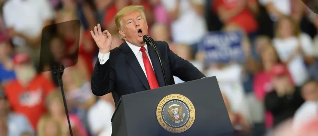The image shows a person speaking at a podium with the presidential seal, addressing a crowd in a public setting.