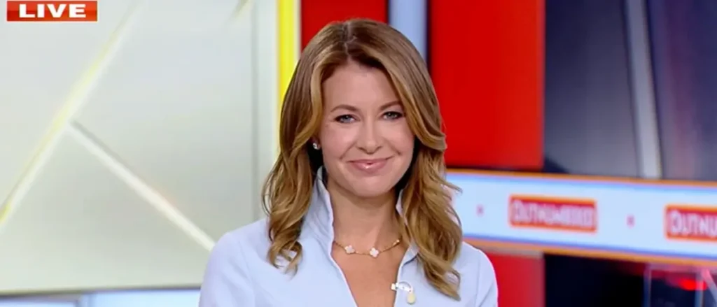 A news anchor is smiling on a television set with a "LIVE" indicator in the corner.