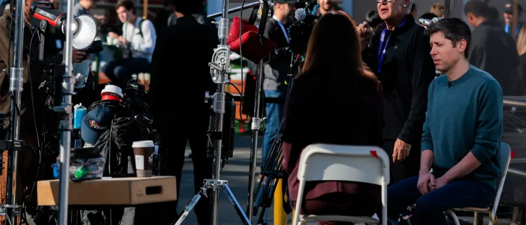 A news crew is preparing for a live broadcast, with equipment and crew members gathered around a seated reporter.