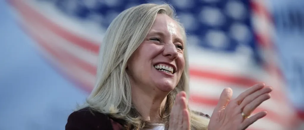 A woman smiles and claps in front of an American flag.