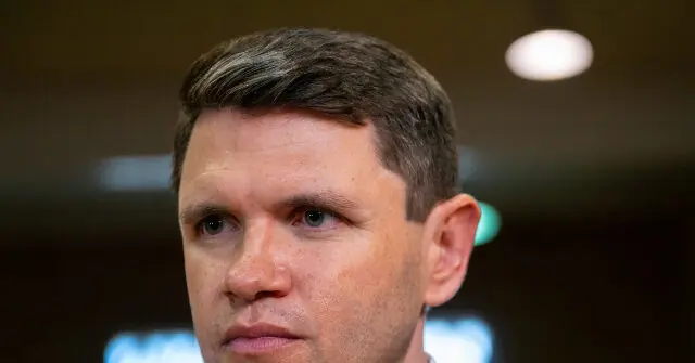 The image shows a close-up of a man with short, neatly styled hair, looking serious and focused.