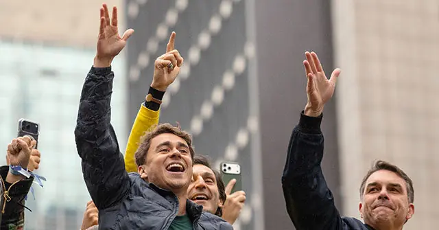 A group of people celebrate and raise their hands in the air, possibly in a public gathering or event.