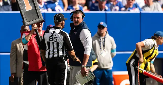 A football coach is seen in a discussion with a referee and other personnel on the sidelines during a game.