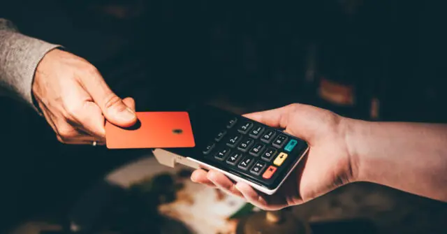A person is using a credit card to make a payment at a point-of-sale terminal.