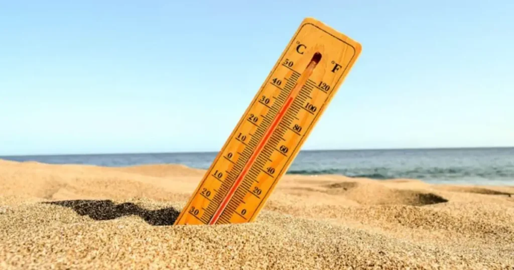 A thermometer stuck in the sand on a beach shows a temperature of around 30°C (86°F).
