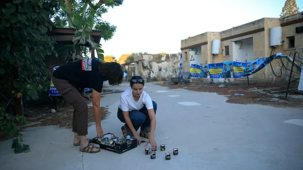 Two individuals are setting up candles on the ground in an outdoor area, possibly as part of a memorial or protest.