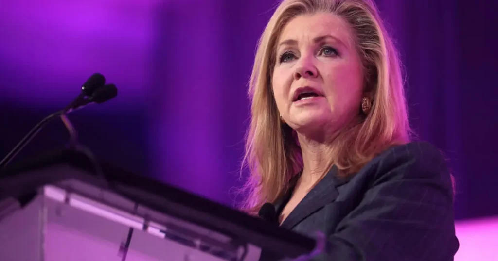 A woman is speaking at a podium in front of a purple-lit background.
