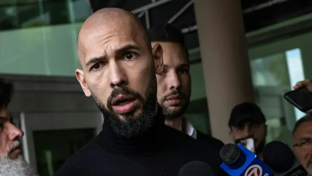 A man with a beard speaks into microphones surrounded by other individuals in what appears to be a press conference or public statement.