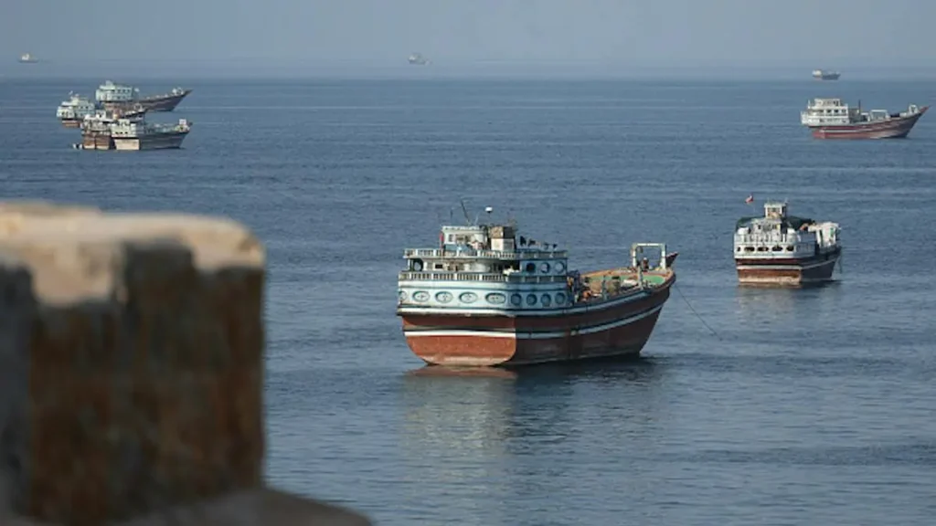 The image shows several boats anchored in calm waters, with a stone structure in the foreground.