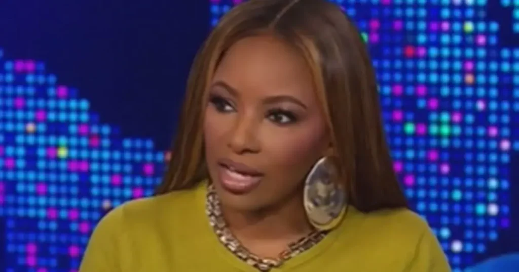 The image shows a person wearing a yellow top and large hoop earrings, set against a colorful, pixelated background.