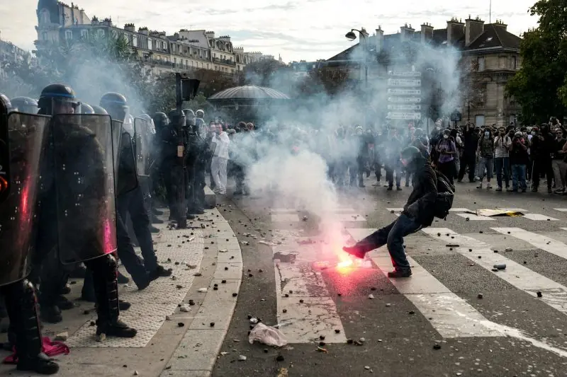 A protester is seen kicking a flare in front of a line of riot police during a demonstration.