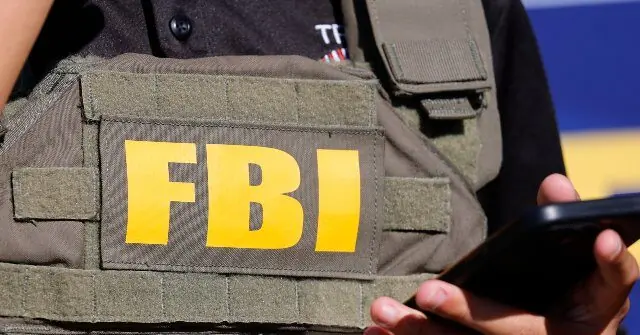 The image shows a person wearing an FBI vest while holding a smartphone.