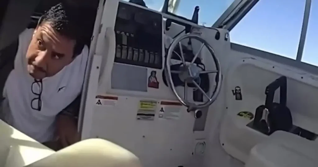 A man is seen inside a boat, leaning over the dashboard, with a steering wheel and various controls visible.