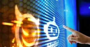 A hand interacts with a futuristic interface displaying a smiling robot icon and the word "Hello!" on a vibrant LED screen.