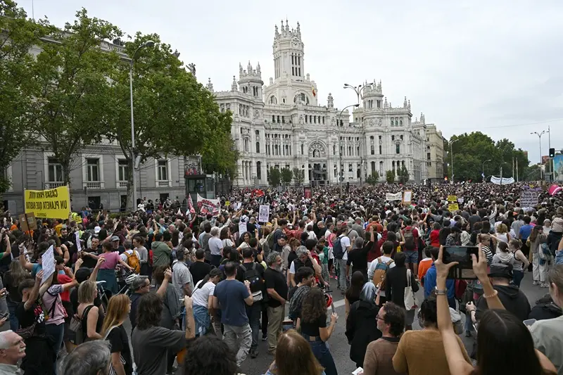 A large crowd gathers in front of a grand building, holding signs and participating in a protest.