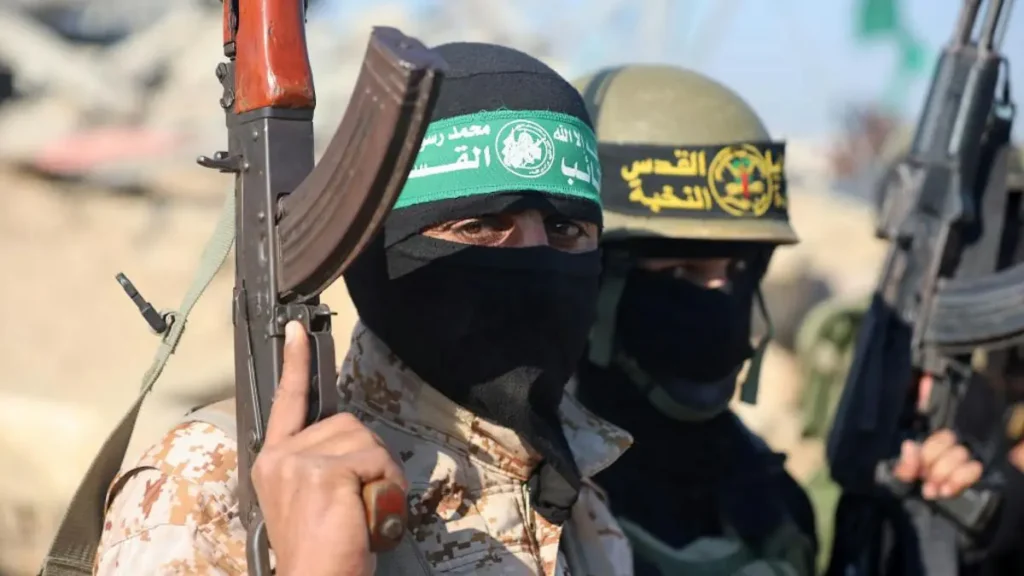 The image shows armed individuals wearing military-style attire and headgear, with one person holding a rifle, suggesting a military or combat-related context.