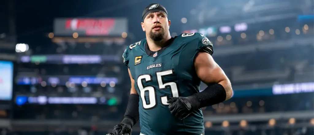 The image shows a Philadelphia Eagles football player wearing jersey number 65, standing on the field during a game.