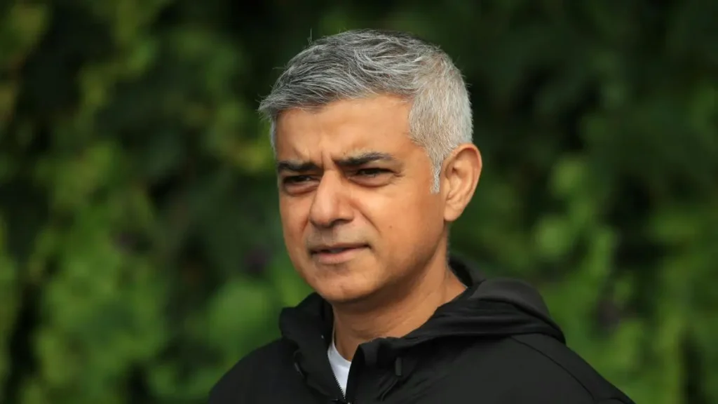 The image shows a person wearing a black jacket, standing outdoors with a blurred green background.