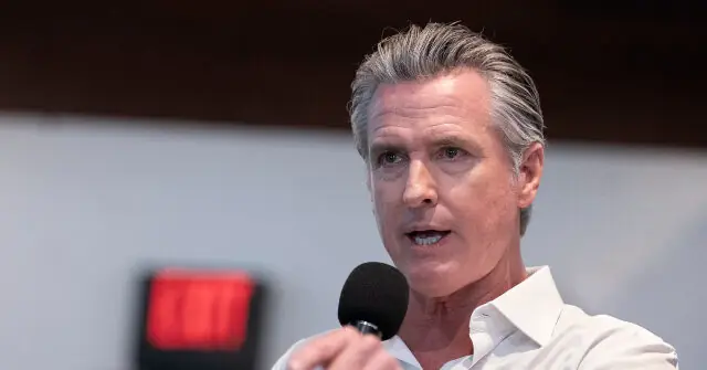 The image shows a man speaking into a microphone, likely during a public address or press conference.