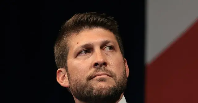 The image shows a close-up of a man with short hair and a beard, looking upwards with a serious expression.