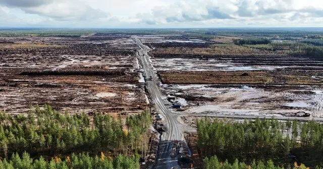 The image shows an aerial view of a large area of land that appears to have been affected by a fire, with charred ground and a road cutting through the devastated landscape.