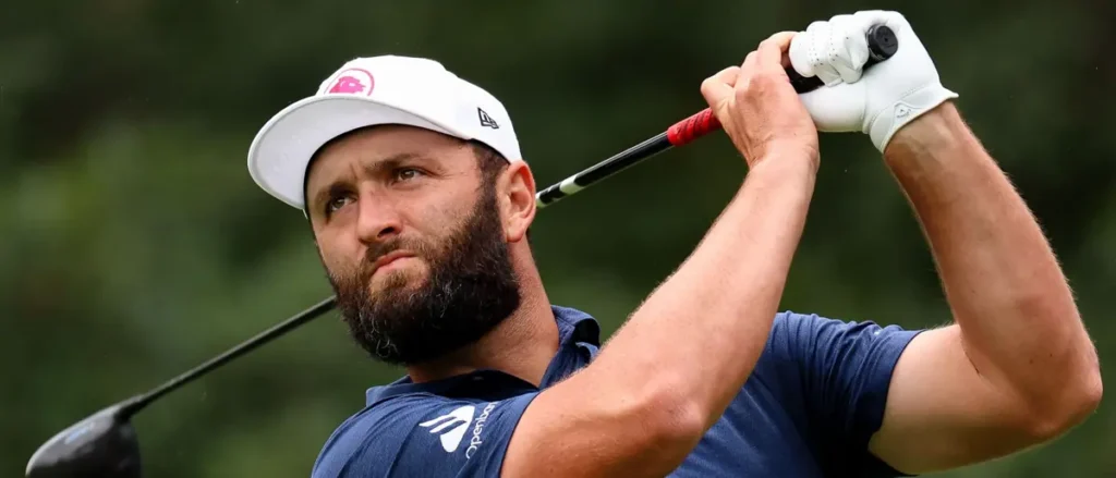 A golfer in a blue shirt and white cap is captured mid-swing during a golf tournament.