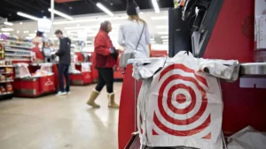 A Target shopping bag is seen on a checkout counter in a store, with customers in the background.