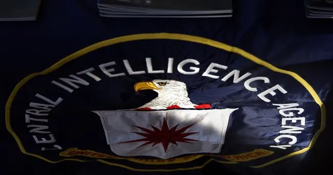 The image shows the emblem of the Central Intelligence Agency (CIA) featuring an eagle and a starburst design.