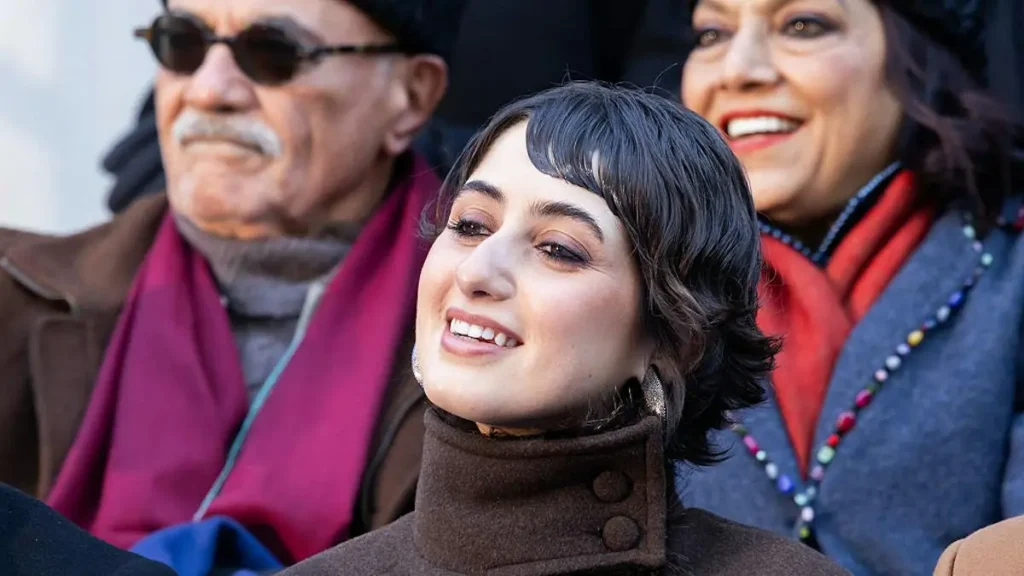 A woman smiles warmly while seated with two other individuals in a public setting.