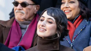 A woman smiles warmly while seated with two other individuals in a public setting.