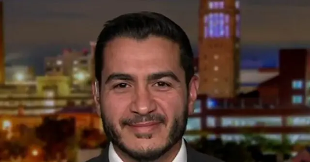 The image shows a man in a suit and tie, smiling, with a cityscape in the background.