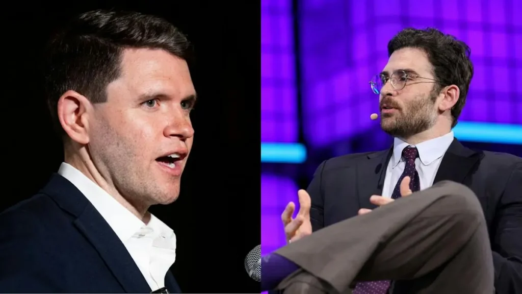 The image shows two men in suits, one speaking into a microphone while the other gestures with his hands, likely during a formal discussion or debate.