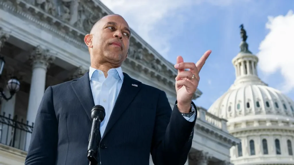 A man in a suit gestures with his right hand while speaking in front of the U.S. Capitol building.
